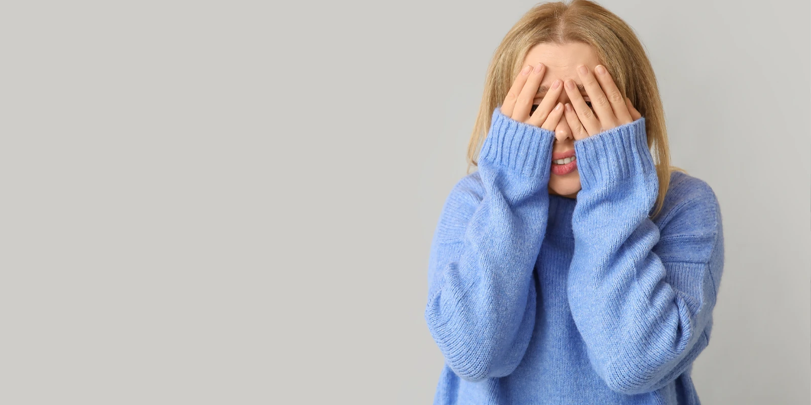 Eine junge Frau, die sich aufgrund ihrer Atembeschwerden schämt und ihr Gesicht mit den Händen bedeckt.
