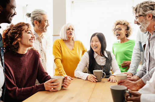 Eine vielfältige Gruppe von Menschen, die an einem Tisch lacht und soziale Interaktion in der COPD-Unterstützung zeigt.