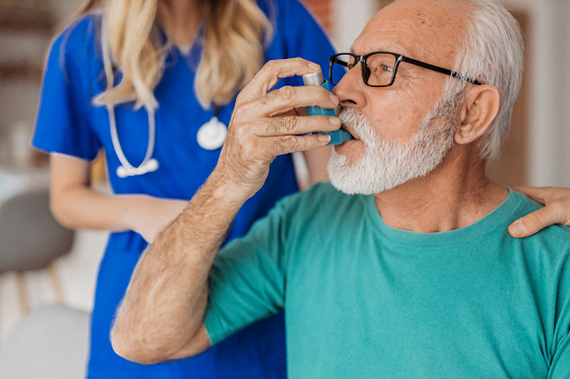 Elderly man using an inhaler under medical supervision, promoting COPD management with Breathment's advanced respiratory care solutions.