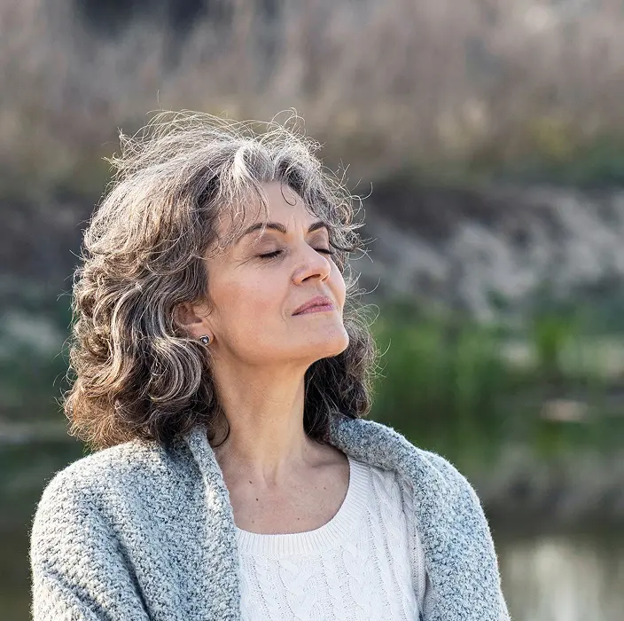 Older woman standing outdoors by a lake